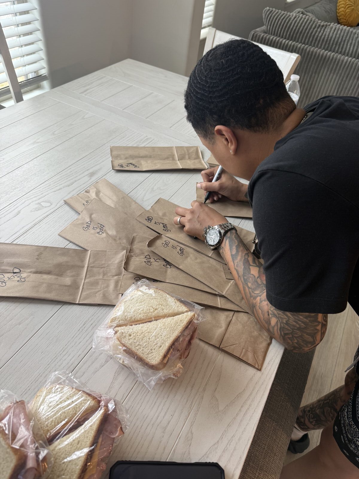 Writing God is Good on paper lunch bags at a prep table