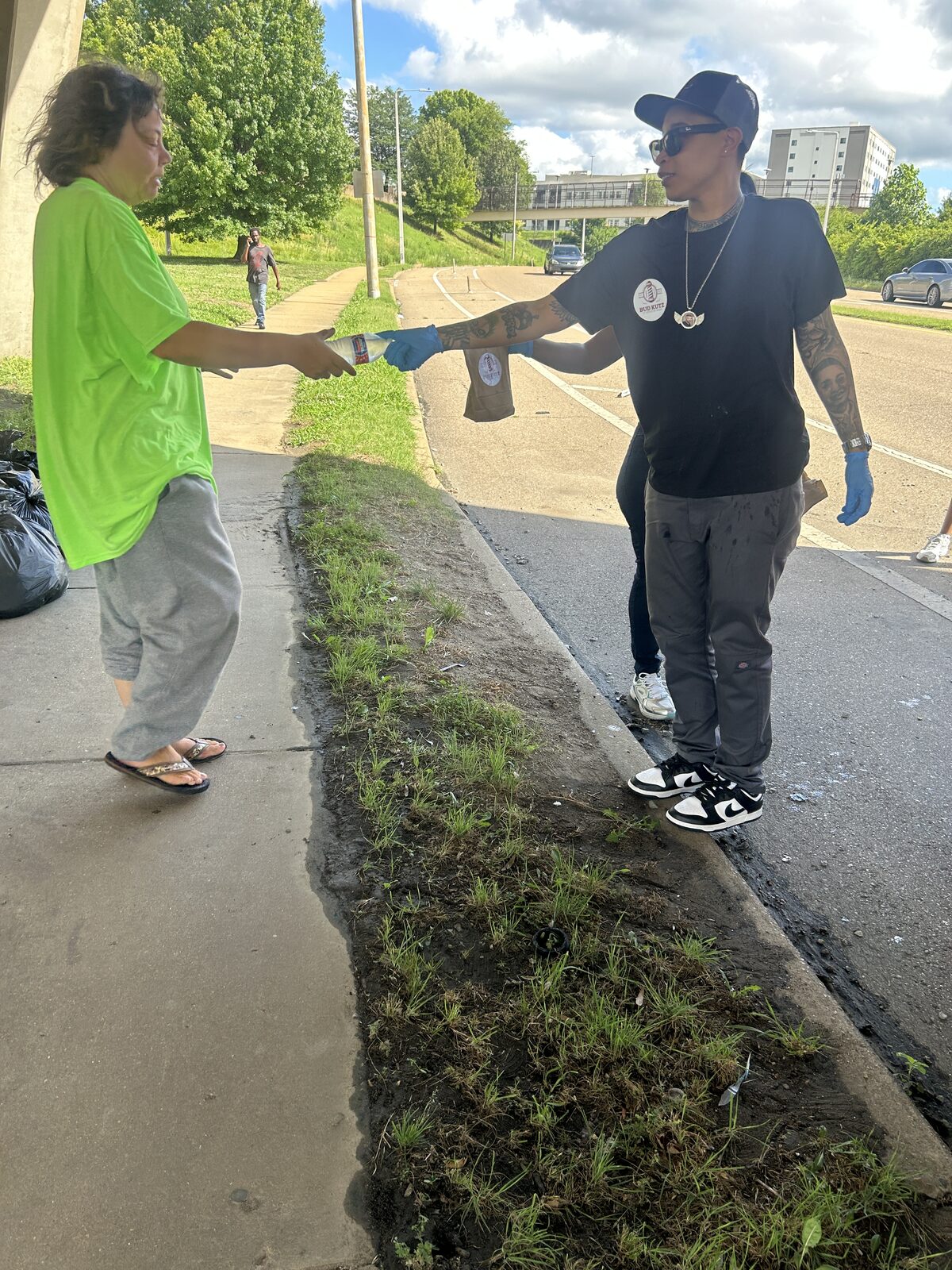 Bud in a Bud Kutz shirt handing water and a lunch bag to a woman on a Memphis street